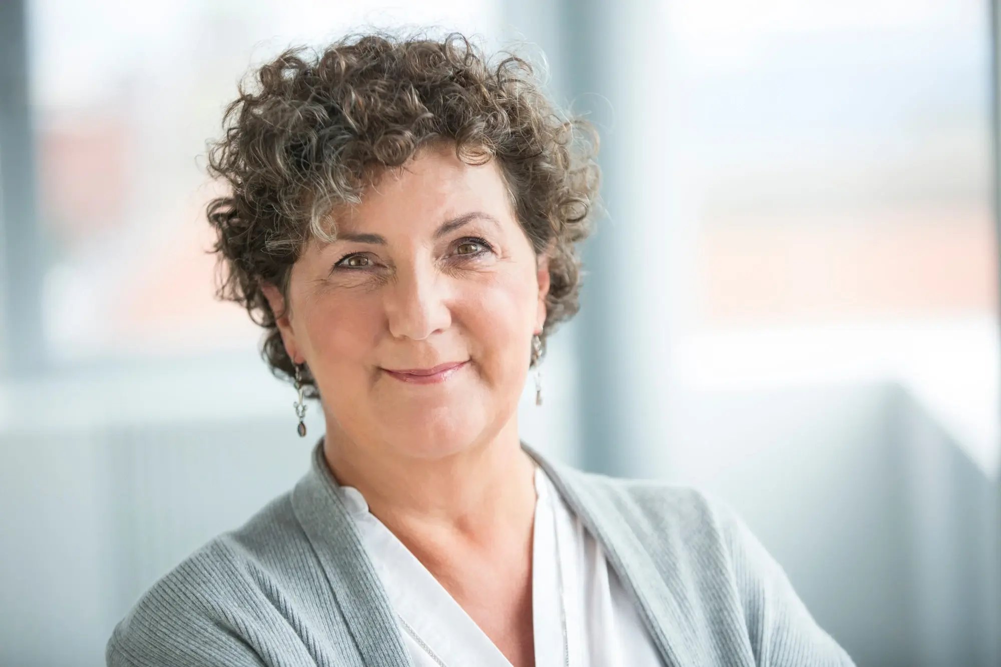 Freundlich blickende Frau (Anja Piel) in heller Kleidung vor unscharfem Hintergrund.