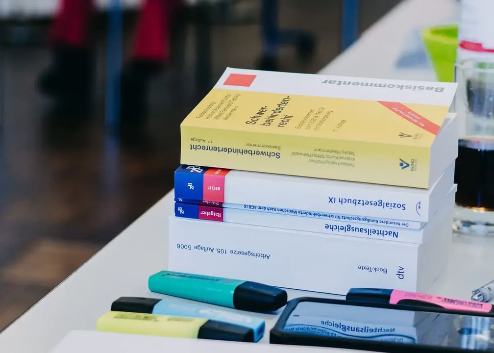 Stapel von Fachbüchern zu Arbeitsrecht und Sozialgesetzgebung auf einem Tisch, daneben mehrere bunte Textmarker.