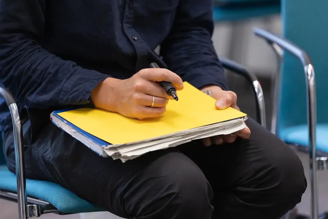 Nahaufnahme einer Person, die auf einem gelben Ordner schreibt, Ordner liegt auf dem Schoß.