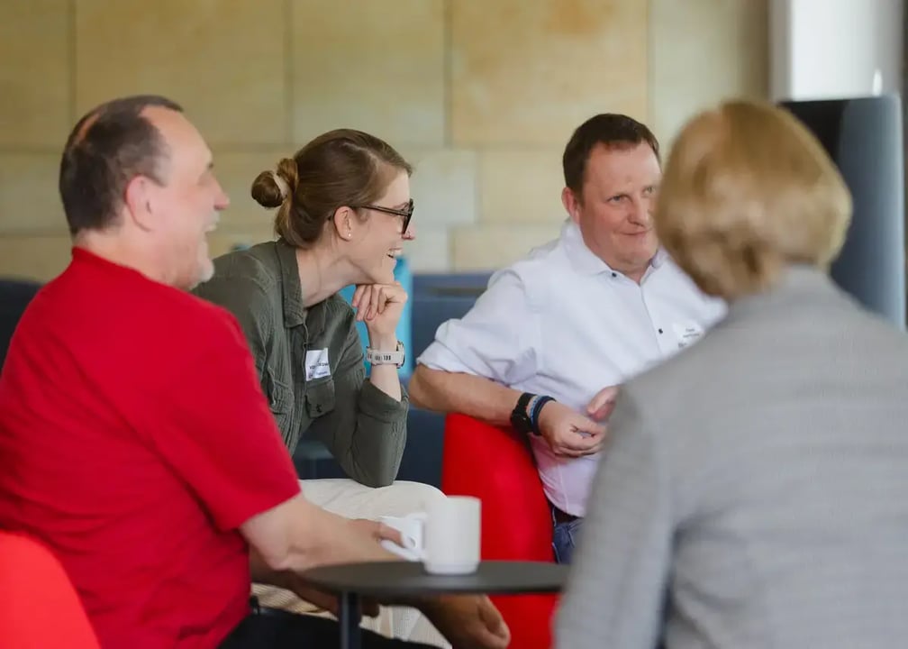 Vier Personen sitzen in einer Gesprächsrunde an einem kleinen Tisch mit Kaffeetassen.