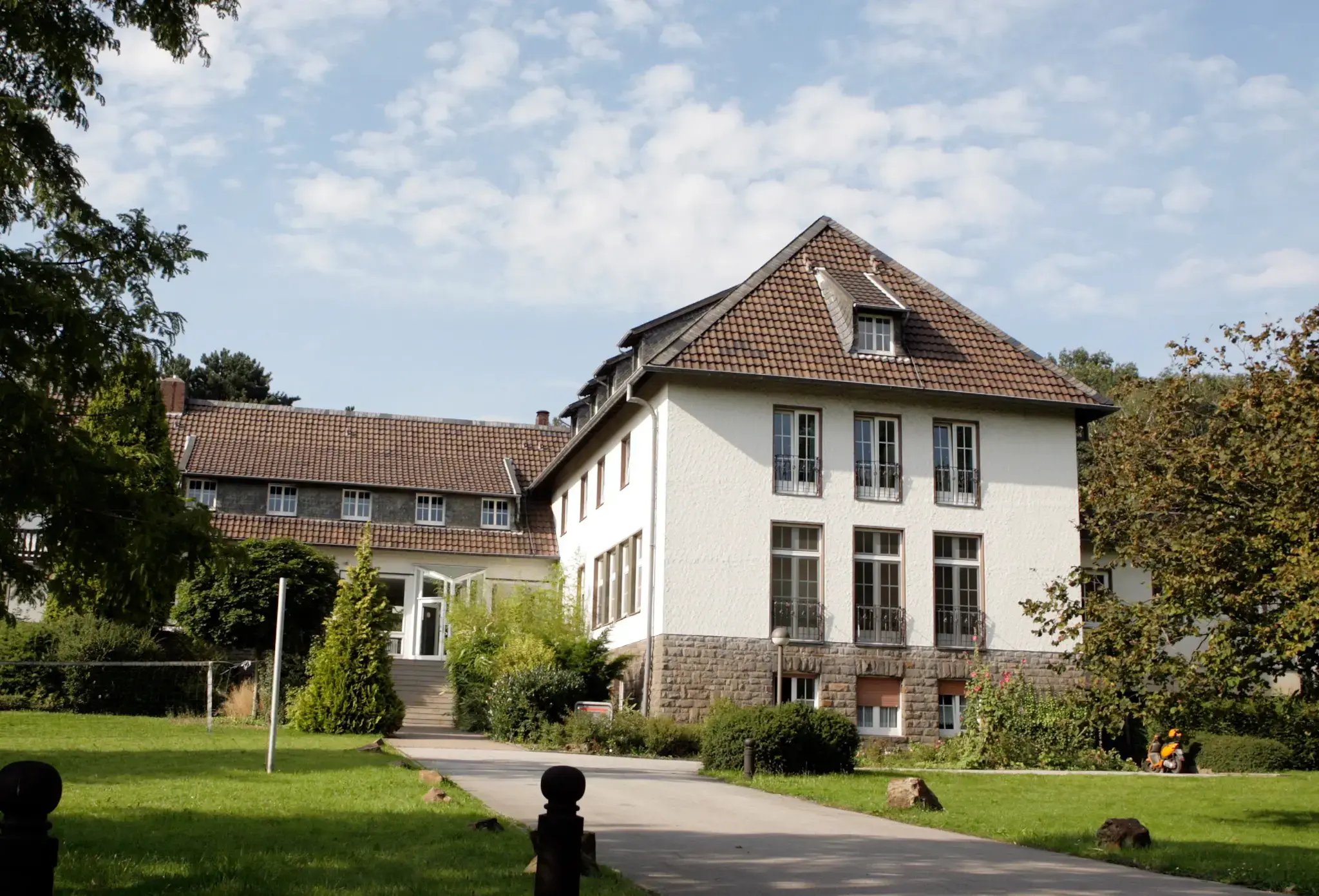 Seminarhaus mit großem Garten und Zufahrtsweg an einem sonnigen Tag.
