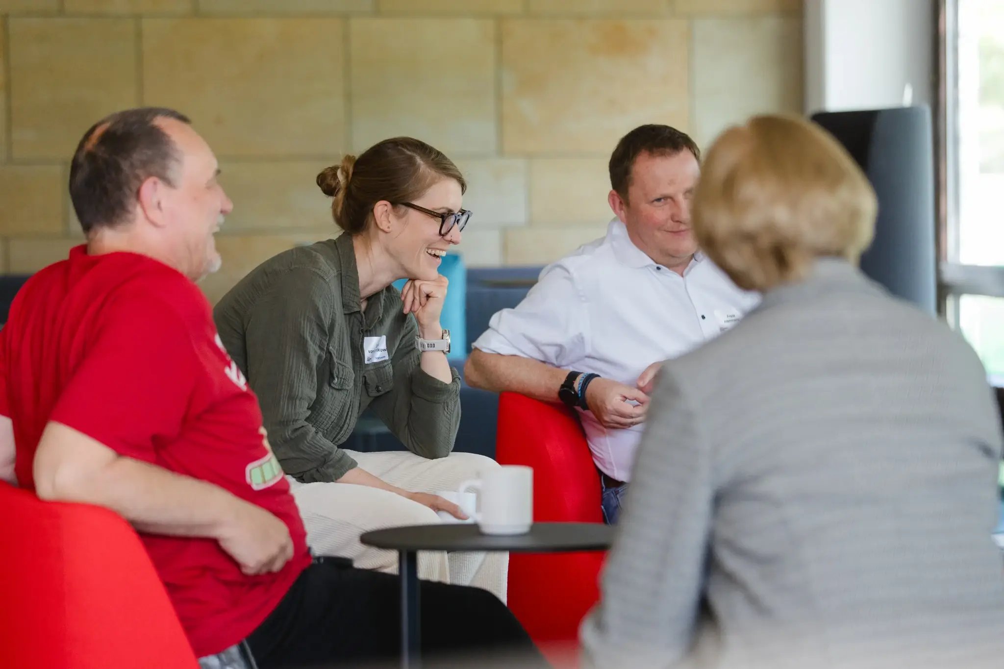 Kleine Gruppe sitzt in Sesseln im Gespräch und lacht in einem Seminarraum.